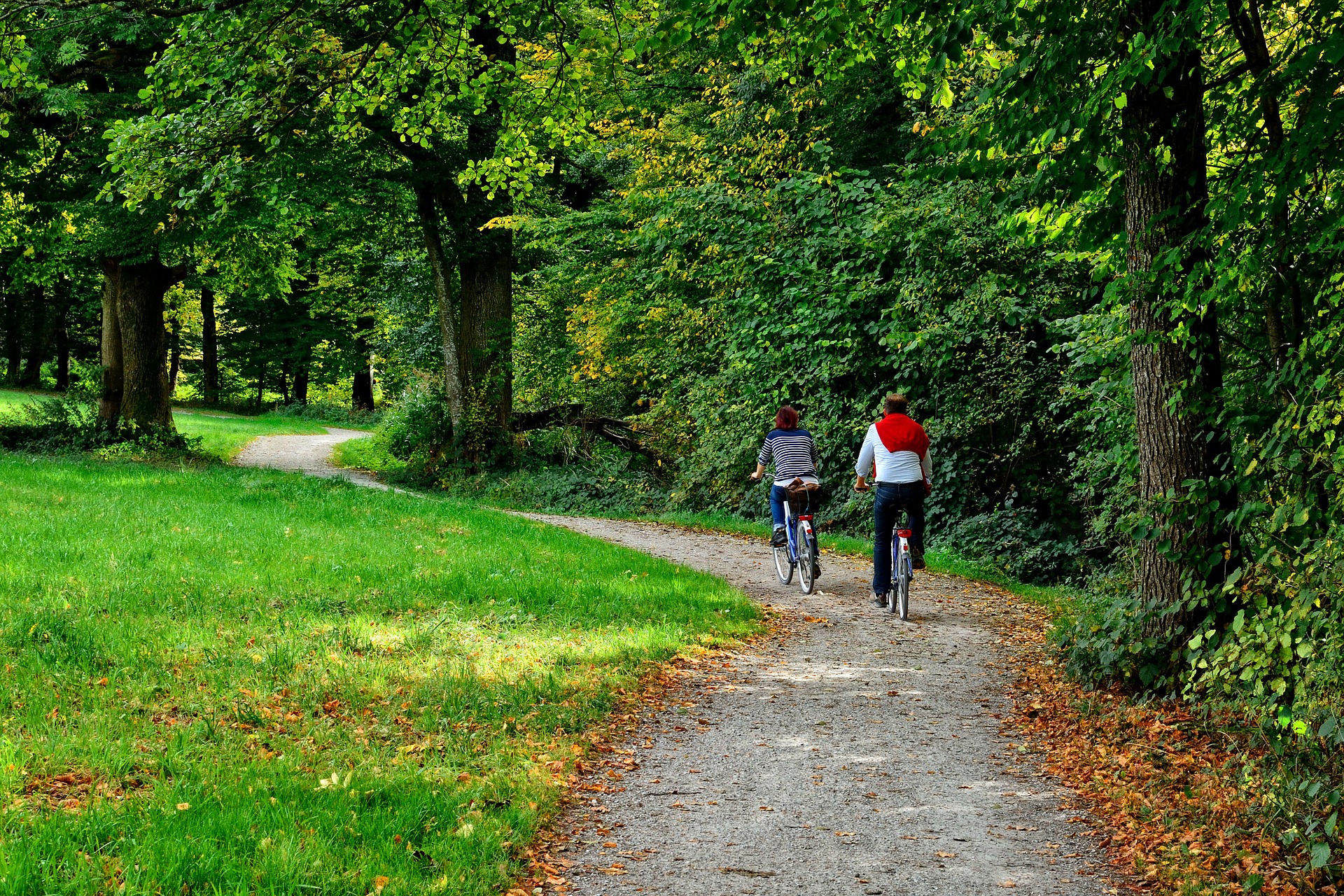 Auf dem Bild sind zwei Radfahrer (eine Frau und ein Mann) zu sehen, die über einen leichten Schotterweg durch einen Park fahren.