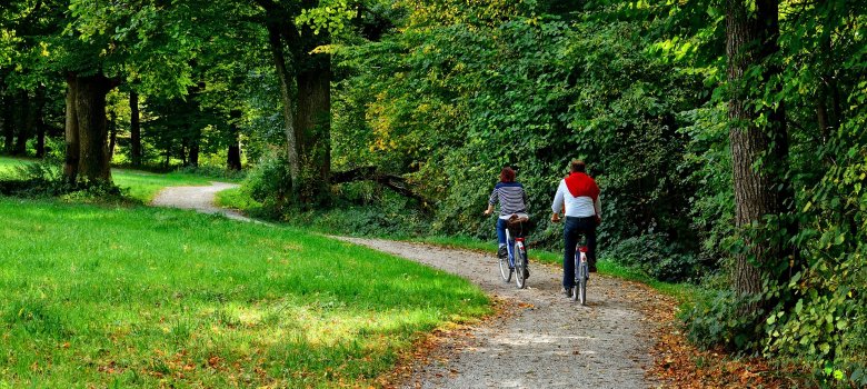 Auf dem Bild sind zwei Radfahrer (eine Frau und ein Mann) zu sehen, die über einen leichten Schotterweg durch einen Park fahren.