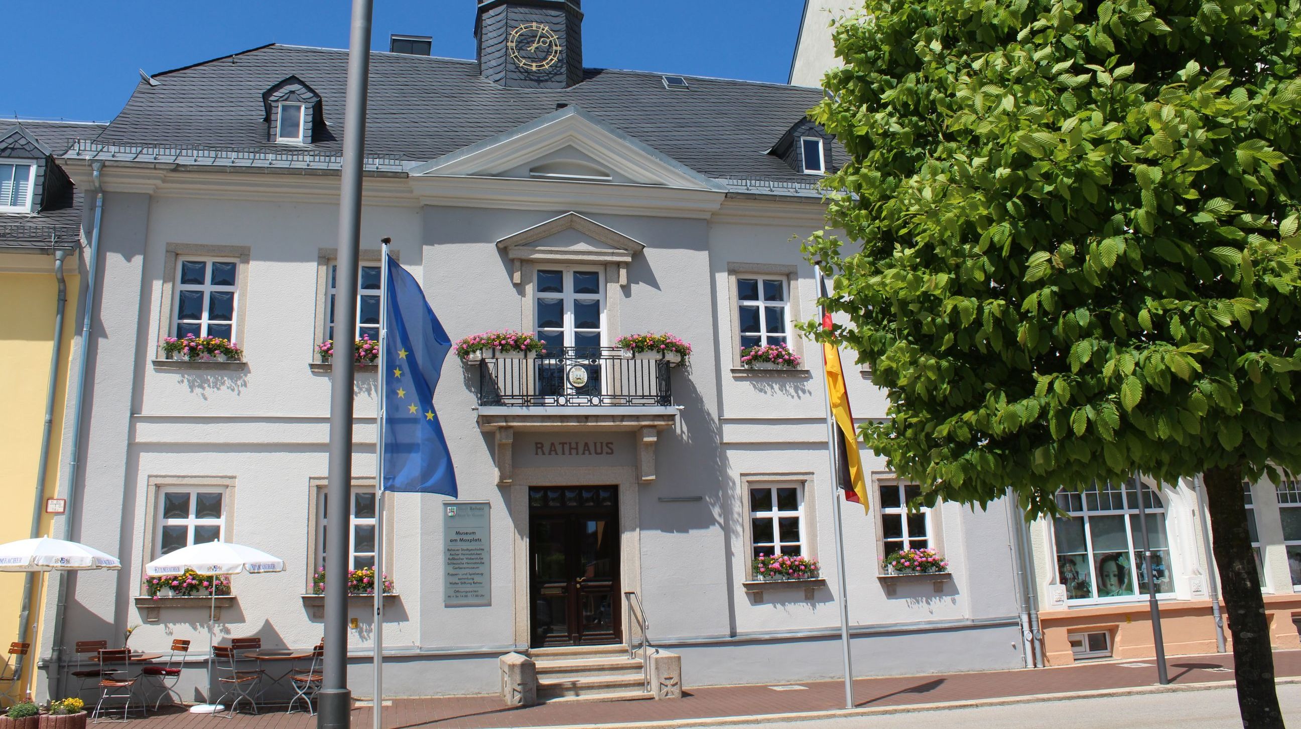Das Bild zeigt das Alte Rathaus am Maxplatz von außen. Davor befinden sich zwei Fahnen, einerseits die europäische Flagge, andererseits die deutsche Flagge.