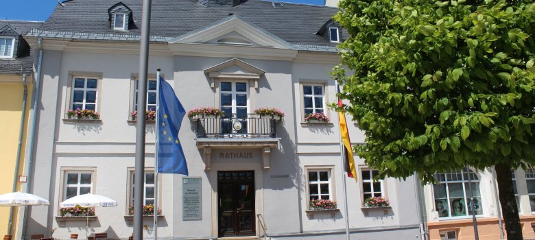 Das Bild zeigt das Alte Rathaus am Maxplatz von außen. Davor befinden sich zwei Fahnen, einerseits die europäische Flagge, andererseits die deutsche Flagge.