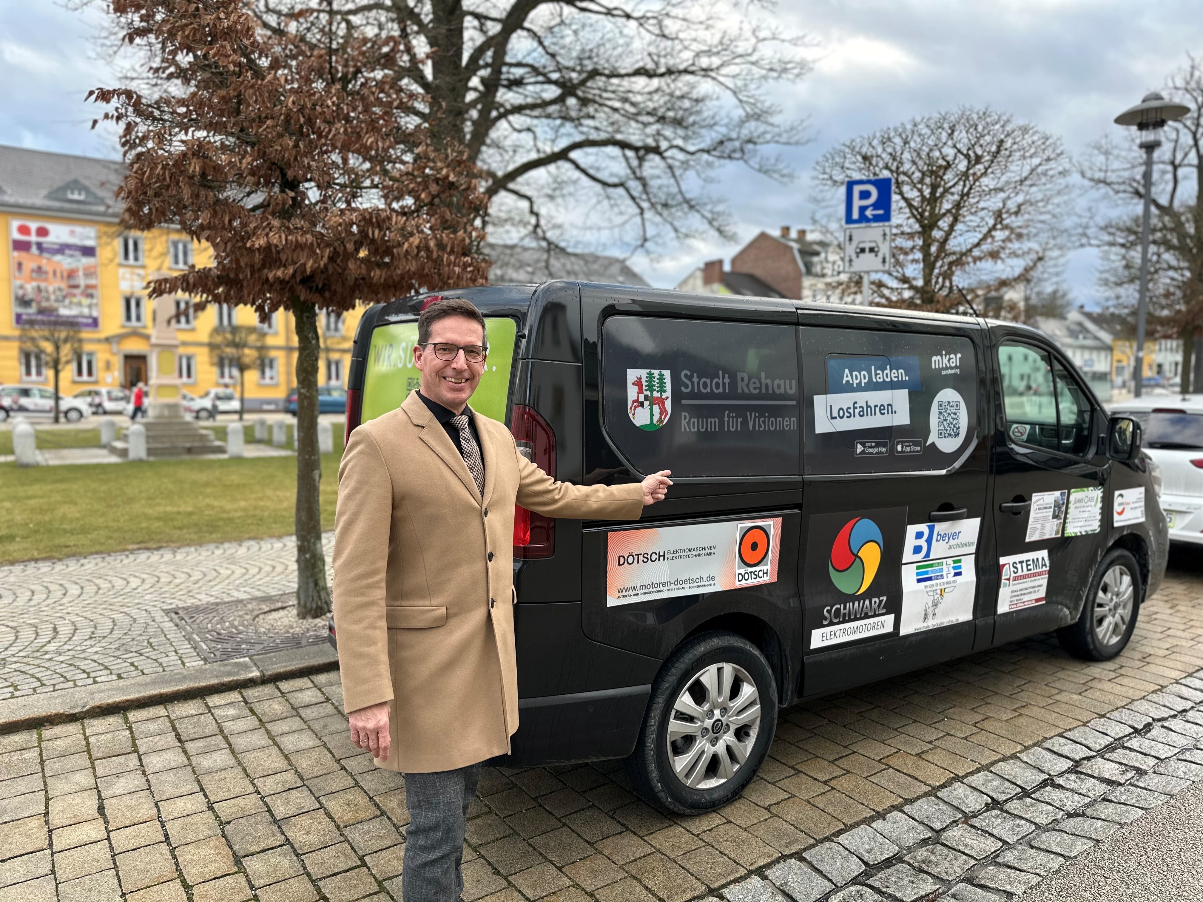 Das Bild zeigt Bürgermeister Michael Abraham vor dem MIKAR der Stadt Rehau, wie er auf das Logo der Stadt Rehau auf dem Auto zeigt.