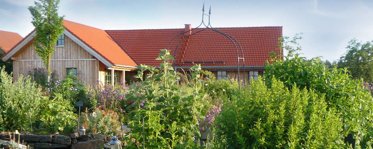Das Bild zeigt das Gebäude des Naturhofs Faßmannsreuth. Davor wachsen viele Pflanzen und Kräuter.
