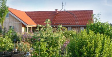 Das Bild zeigt das Gebäude des Naturhofs Faßmannsreuth. Davor wachsen viele Pflanzen und Kräuter.