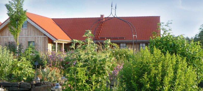 Das Bild zeigt das Gebäude des Naturhofs Faßmannsreuth. Davor wachsen viele Pflanzen und Kräuter.