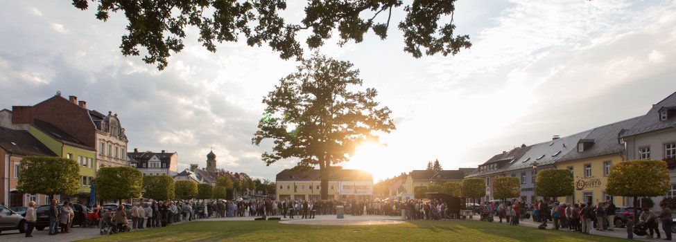 Das Bild zeigt viele Personen bei einer Veranstaltung am Maxplatz. Die Sonne ist kurz vor dem Verschwinden. Zu sehen sind in der Mitte des Maxplatzes einige Musiker.