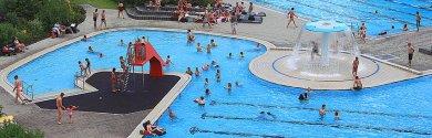 Das Bild zeigt das Spaßbecken im Rehauer Freibad mit einigen Kindern, die sich gerade daneben oder darin befinden.
