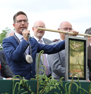 Das Bild zeigt Bürgermeister Abraham am Mikrofon mit der Ehrenplakette des Europarates in der anderen Hand auf der Ehrentribüne beim Rehauer Wiesenfest 2019.