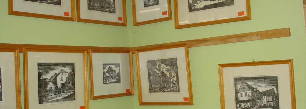 Das Bild zeigt verschiedene Zeichnungen in Holzrahmen die an der grünen Wand befestigt sind.