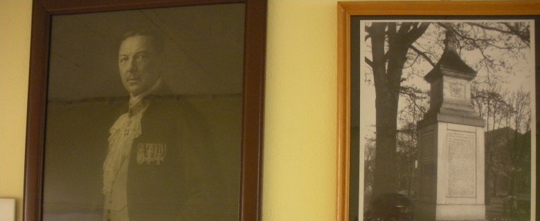 Das Bild zeigt zwei Bilder auf einer gelben Wand. Das linke zeigt Hans Grässel, das rechte ein Denkmal.