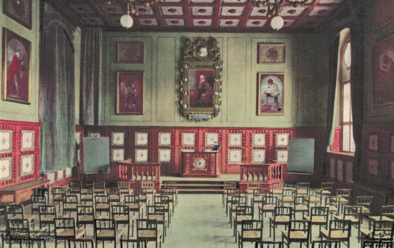 Das Bild zeigt einen alten Saal mit zahlreichen Stühlen vor einem Podest.